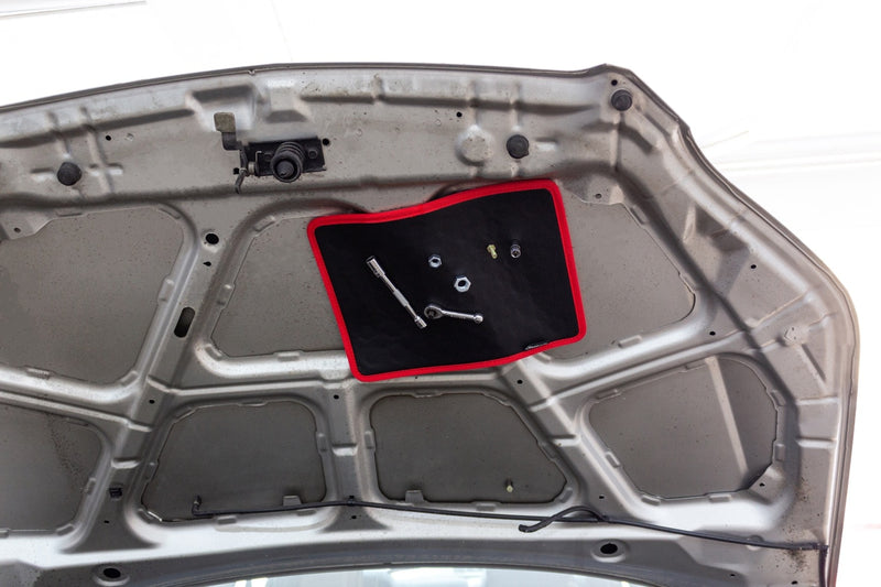 Magnetic tool mat holding tools and nuts and bolts upside down under the hood of a vehicle